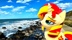 Size: 1200x676 | Tagged: safe, artist:nekokevin, sunset shimmer, pony, unicorn, female, irl, mare, ocean, photo, plushie, rock, smiling, smug, solo