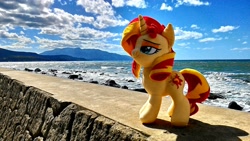 Size: 1200x675 | Tagged: safe, artist:nekokevin, sunset shimmer, pony, unicorn, cloud, female, irl, mare, ocean, photo, plushie, rock, smiling, smug, solo