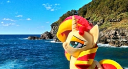 Size: 1199x651 | Tagged: safe, artist:nekokevin, sunset shimmer, pony, unicorn, female, irl, mare, ocean, photo, plushie, rock, smiling, smug, solo