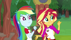 Size: 1280x720 | Tagged: safe, derpibooru import, screencap, rainbow dash, sunset shimmer, equestria girls, legend of everfree, camp everfree outfits, clothes, duo, female, pointing, scenery, shorts, sun, tree, wristband