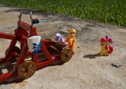 Size: 1519x1082 | Tagged: safe, apple bloom, applejack, blind bag, catapult, cowtapult, irl, outdoors, photo, tiarabuse, tied up, toy