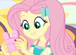 Size: 1507x1080 | Tagged: safe, screencap, fluttershy, better together, equestria girls, holidays unwrapped, camera, canterlot mall, chair, clothes, cropped, cute, dashing through the mall, dress, female, geode of fauna, hairclip, happy, jewelry, looking down, magical geodes, mall, necklace, present, shyabetes, sitting, solo