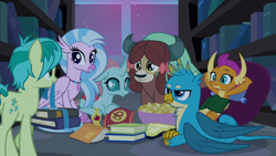 Size: 1280x720 | Tagged: safe, derpibooru import, screencap, gallus, ocellus, sandbar, silverstream, smolder, yona, classical hippogriff, dragon, earth pony, griffon, hippogriff, pony, yak, school raze, book, bookshelf, chips, cutie mark, dragoness, female, food, male, smiling, student six, tail, teenager, wings