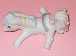 Size: 579x426 | Tagged: safe, derpibooru import, photographer:absol, first born, earth pony, pony, g1, adoraborn, bow, cute, female, irl, irl photo, lying down, mare, multicolored hair, my little pony logo, photo, porcelain, porcelain figurine, rainbow hair, smiling, tail, tail bow, toy