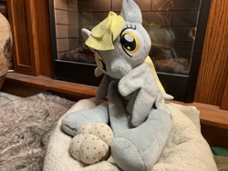 Size: 4032x3024 | Tagged: safe, artist:ciaran, derpibooru import, derpy hooves, bed, female, fireplace, food, grooming, irl, looking at you, muffin, photo, photography, plushie, preening, rug, welovefine