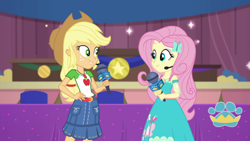 Size: 1000x563 | Tagged: safe, derpibooru import, screencap, applejack, fluttershy, best in show: the victory lap, better together, equestria girls, applejack's hat, clothes, cowboy hat, dress, geode of fauna, geode of super strength, hand on hip, hat, looking at each other, magical geodes, microphone, skirt, smiling