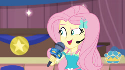 Size: 3410x1920 | Tagged: safe, derpibooru import, screencap, fluttershy, best in show: the victory lap, better together, equestria girls, best in show logo, female, geode of fauna, hairpin, jewelry, magical geodes, microphone, necklace, open mouth, smiling, solo