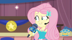 Size: 3410x1920 | Tagged: safe, derpibooru import, screencap, fluttershy, best in show: the victory lap, better together, equestria girls, best in show logo, female, geode of fauna, hairpin, jewelry, magical geodes, microphone, necklace, smiling, solo