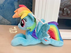 Size: 4062x3046 | Tagged: safe, derpibooru import, rainbow dash, pegasus, pony, g4, irl, lying down, merchandise, official, photo, plushie, pony plushie, reesee, side view, smiling, solo, spread wings, text, wings