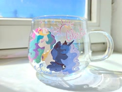 Size: 4000x3000 | Tagged: safe, artist:mirtash, derpibooru import, princess celestia, princess luna, alicorn, pony, g4, blue coat, blue mane, blue text, colored eyelashes, colored pinnae, crown, curly hair, curly mane, duo, duo female, ear fluff, ears, ethereal mane, eyes closed, eyeshadow, female, folded wings, height difference, high res, horn, irl, jewelry, long horn, makeup, mare, mug, mug design, multicolored mane, multicolored tail, peytral, photo, pink text, profile, purple eyelashes, regalia, royal sisters, siblings, sisters, sparkles, tail, text, tiara, unicorn horn, wavy mane, white coat, wing fluff, wings